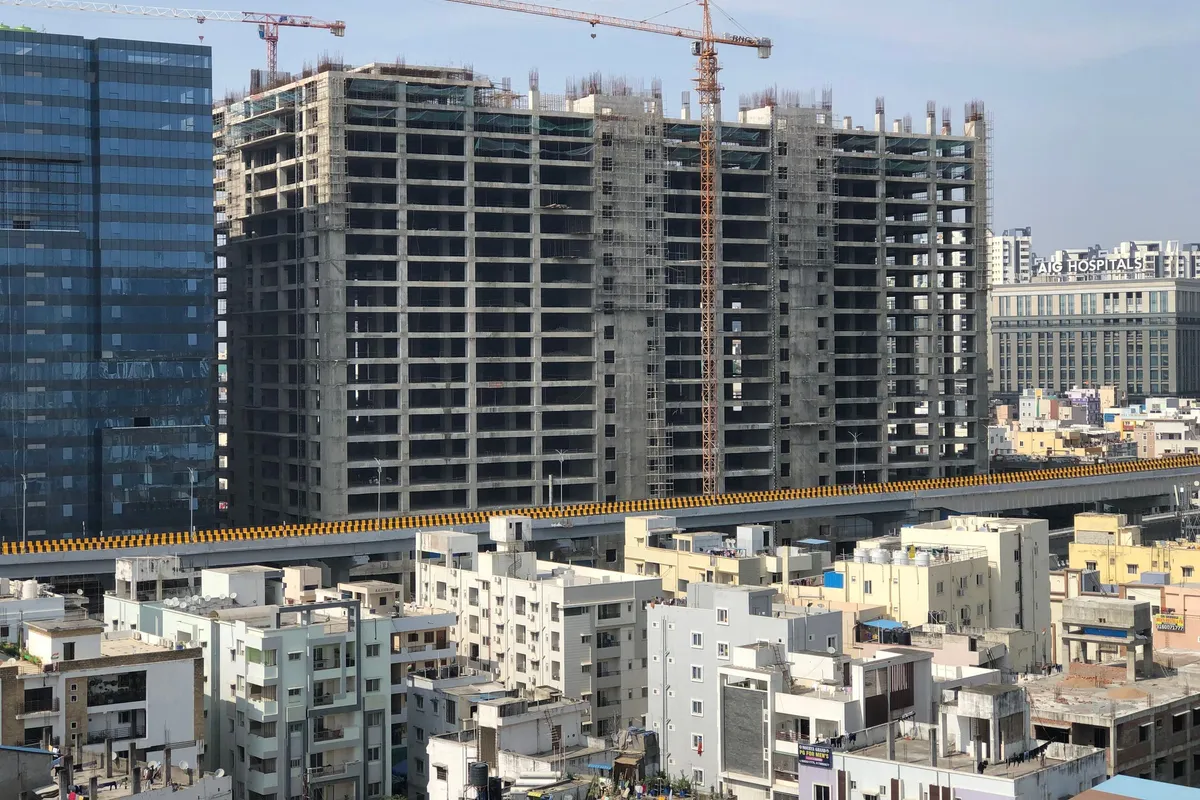 High-rise apartment building under construction with tower cranes above low-rise city housing