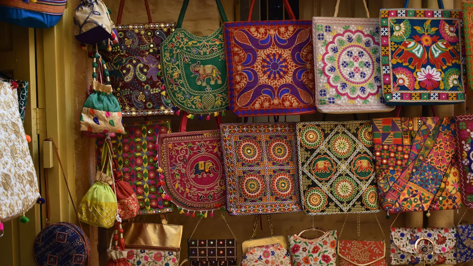Colourful hand-embroidered handbags and pouches hanging on display at an Indian handicraft stall