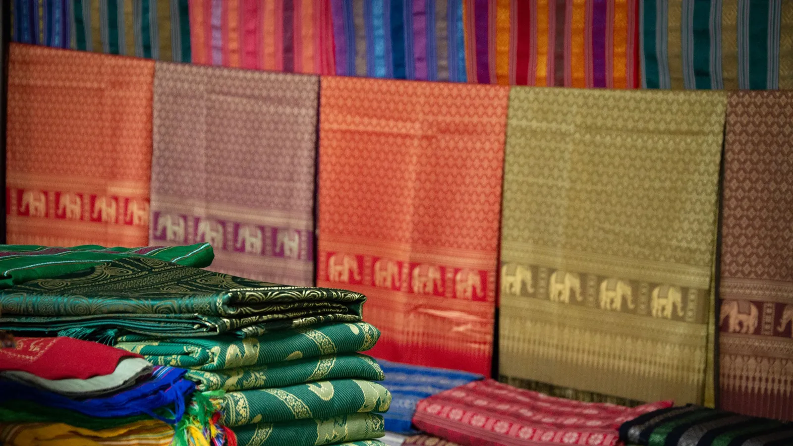 Shelves of folded handloom sarees and silk fabrics in rich colours stacked in a textile store