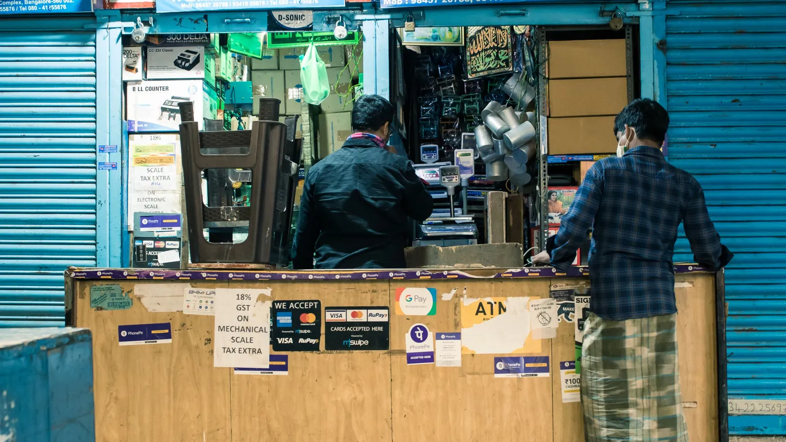Customers standing at a small Indian shop counter with UPI and card payment signs on the front