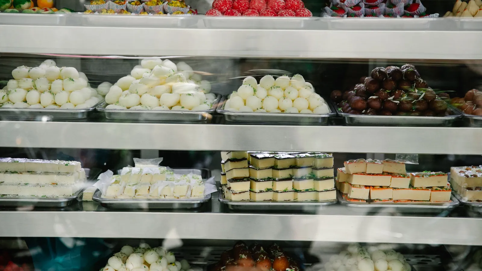 Glass display counter of an Indian sweet shop with trays of rasgulla, gulab jamun and barfi