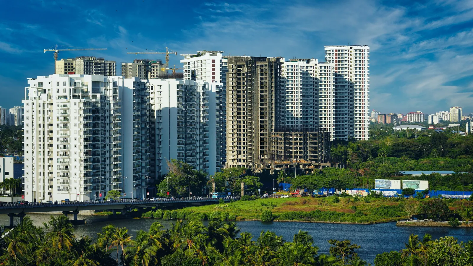 Modern residential apartment towers beside a lake and green trees in an Indian city